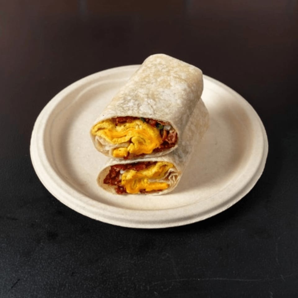 Two halves of a breakfast burrito, filled with scrambled eggs and bacon, on a white plate.