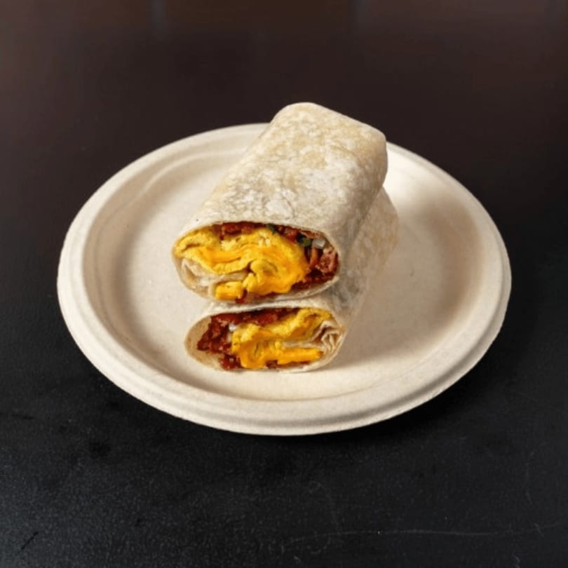 Two halves of a breakfast burrito, filled with scrambled eggs and bacon, on a white plate.