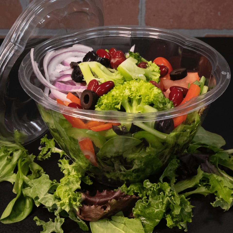 Fresh deli salad in a clear plastic container with lettuce, broccoli, onions, olives, and kidney beans.