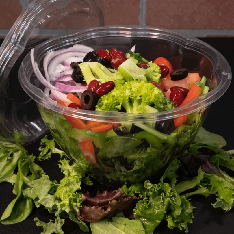 Fresh deli salad in a clear plastic container with lettuce, broccoli, onions, olives, and kidney beans.