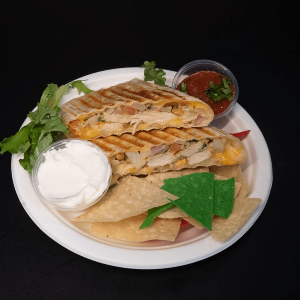 Grilled quesadilla with chicken, cheese, onions, salsa, sour cream, and tortilla chips on a white plate.