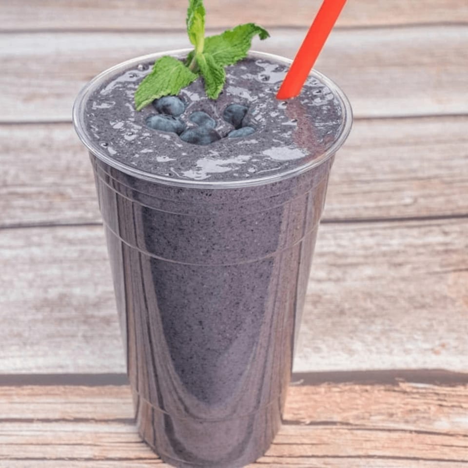Blueberry smoothie with fresh blueberries, mint, and a red straw on a wooden table.