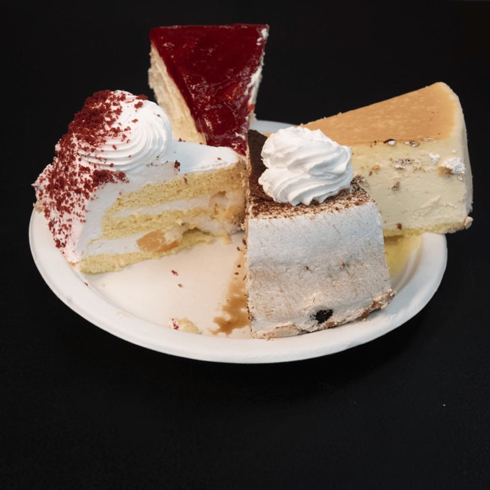 A white plate holds four slices of cake: red velvet, strawberry, cheesecake, and chocolate.